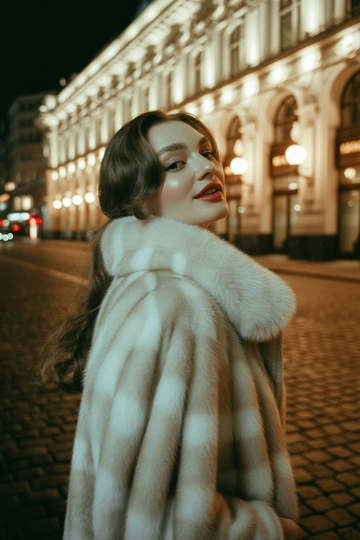 Женщина на улице Москвы у входа в театральное здание, одета в длинную белую норковую шубу с объемным воротником и изысканным блеском меха. В среднем плане она слегка откидывает голову назад и улыбается в камеру, распущенные волосы, ретро-макияж с акцентом на губы, стиль старого журнала.