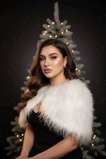 Праздничная студийная фотосессия. Женщина одета в черное вечернее платье на тонких бретелях, с белой пушистой накидкой из перьев. Фон — градиент от черного к тёмно-серому, мягкий тёплый направленный свет сбоку, лёгкие светлые частицы в воздухе создают эффект падающего снега. Позади стоит минималистичная рождественская ель, украшенной только гирляндой тёплого света. Атмосфера — элегантная, глянцевая, как для зимней рекламной кампании или обложки журнала. Реалистичный стиль, чистая кожа, аккуратный макияж, акцент на блеске украшений и фактуре перьев. Волосы длинные, блестящие и густые. Очень крупный план. Кадр сосредоточен на лице и линии плеч, перья частично закрывают подбородок. Свет тёплый, падает сбоку, выделяя ресницы и текстуру кожи. Атмосфера кинематографичная, загадочная.