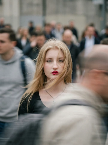     Cinematic motion-blur photography shot on a Leica SL3 with a 50mm Summilux at f/2.8, captured from a chest-level frontal angle using slow shutter panning. Lighting setup: flat overcast daylight acting as soft diffusion, allowing long blur trails without harsh contrast. Color tone: muted concrete greys and pale skin neutrals inspired by A24 films.
Subject: a The young woman from the reference has light hair frozen mid-flight across her face, porcelain skin with a subtle flush catching the warm light, light green eyes locked onto the camera in piercing stillness amidst the chaos, lips accentuated by a bold cherry-red lipstick that creates a focal point of saturated color, wearing understated fashion.
Crowd action: hundreds of commuters rushing past in all directions, bodies stretched into smooth horizontal and diagonal blur. Emotion: quiet rebellion through stillness. Aesthetic: editorial calm vs chaos. Post: clean motion physics, fine grain, no glitches, no face distortion, no warped anatomy. --ar 9:16 -- raw
