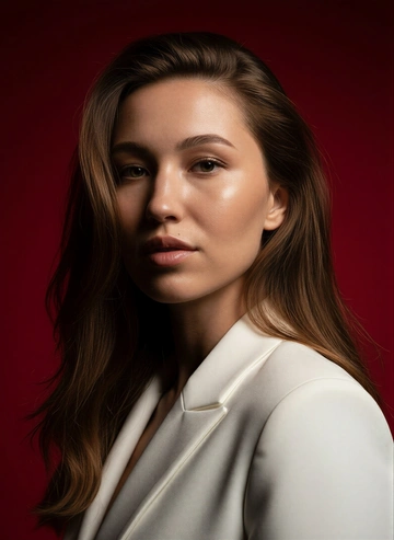 Создай портрет, используя те же черты лица (на основе загруженного фото), характеризующийся резким кинематографическим освещением и интенсивным контрастом. Снятый с немного нижнего ракурса, направленного вверх, что подчеркивает линию подбородка и шеи модели, этот портрет производит впечатление доминантности и скульптурной элегантности. Фон — глубокий, насыщенный малиново-красный, создающий яркий визуальный контраст со сияющей кожей модели и темной одеждой.