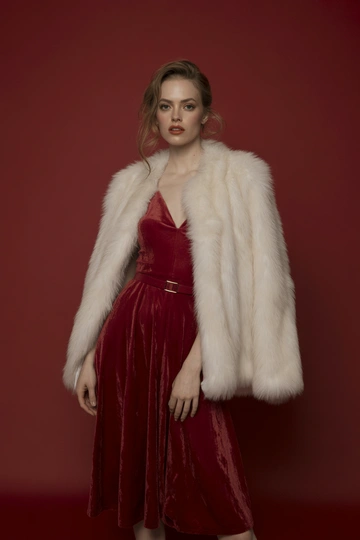 Женщина в студии на красном фоне в роскошной белой шубе, под шубой алое бархатное платье миди с тонким поясом. Стоит в уверенной позе, смотрит прямо в камеру, макияж гламурный с акцентом на губы, распущенные волосы струятся по плечам, образ праздничный и яркий.