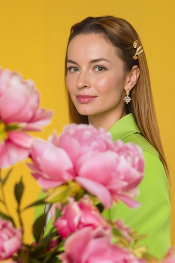 Studio waist-length portrait of a 35-year-old woman in the style of a fashion photo shoot for a fashion magazine. The background is yellow, clean, slightly muted shade. The woman is wearing a bright green jacket. In her ears are earrings made of shining gold with diamonds that shimmer and shine. Her makeup is done in warm green and yellow tones that emphasize the color of her eyes, the emphasis is on the eyes. There is a slight blush on her face. In the foreground of the photo are large lush pink peonies in blur, which partially cover the woman's face and shoulders, the peonies cast beautiful shadows on the woman's face. The woman looks straight into the camera with a light playful smile. The pose is natural, slightly turned half-turned. The atmosphere of the picture is fresh, bright and cheerful. The color scheme is warm, with a predominance of soft pink and yellow shades. The hair is beautifully styled, they are straight and long, the hair color is dark blond. In the hair is a gold hairpin. Camera: Canon 5 R Markt 2, 50mm f 1.8 lens with emphasis and focus on the face. Sharp photo with visible pores on the face and detailed skin texture, small wrinkles and freckles under the eyes. Photorealism, cinematic, glamour photography, perfect natural retouching, 8k, fresh face with even skin tone.