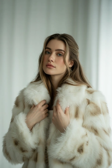Женщина в студии на светлом фоне, в роскошной белой шубе с широким пушистым воротником из длинного меха. Стоит в среднем плане, прямой взгляд в камеру, волосы распущены, легкий естественный макияж подчеркивает свежесть образа. Вдохновлено эстетикой старых модных журналов.