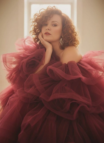 Создай изображение меня
Максимально сохрани мою внешность и прическу
Редакционный портрет красивой женщины из журнала высокой моды, она тонула в объемном пышном бардовом платье из полупрозрачной органзы и тюля — много слоев, оборок и летящих складок, ткань обволакивает тело и лицо по краям; бархатистая загорелая кожа, естественный нюдовый макияж, цвет волос как на фото, элегантные серьги-люстры. Размытый, мечтательный пленочный фильтр: мягкое рассеивание, размытие по краям, кинематографический блум, теплые янтарные и кремовые тона, легкая дымка в воздухе. Поза: крупный план на 3/4, корпус слегка наклонен вперед, кисть на лице, пристальный взгляд в камеру. Освещение: мягкий рассеянный естественный свет из окна, теплый ободочный свет

