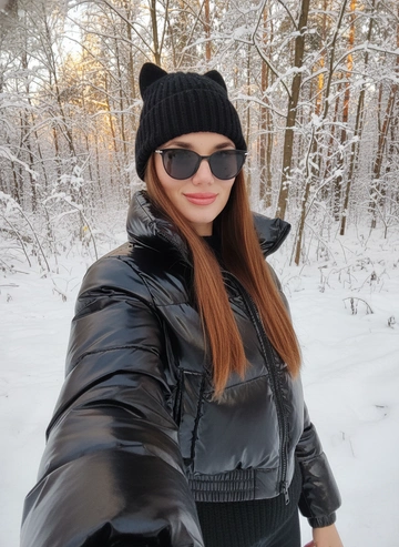 Не меняй черты лица Создайте гиперреалистичное изображение девушки, которая делает селфи с вытянутой рукой, кисть не видно как будто она держит камеру. Она носит укороченную объёмную чёрную лаковую зимнюю куртку с высоким горлом, на голове черная зимняя шапка с ушками кошки, а её взгляд с легкой улыбкой, она полубоком к камере. На лице очки тонкие черные солнцезащитные стильные 
Кисть руки не видна, так как она держит телефон Куртка утеплённая с высокой талией, создавая стильный зимний образ. 
Фото в золотой час Волосы прямые 
Фон зимний лес