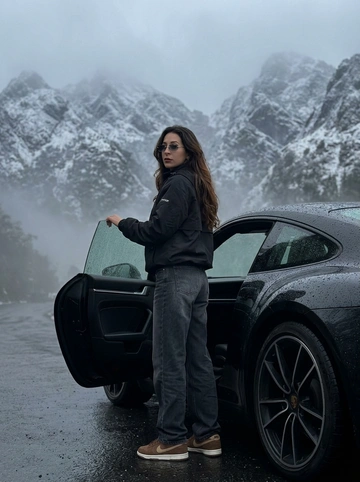 Не менять черты лица человека с исходного фото. Человек рядом с стоит рядом с машиной, машина на горной дороге, дорога мокрая от тумана, машина в каплях от тумана. Чёрный анорак Planta Rosa, маленькие чёрные солнцезащитные очки без оправы, мешковатые серо-чёрные джинсы с низкой посадкой, длинные, коричневые замшевые кроссовки Nike Dunk, руки в карманах. Машина без номеров. Фон — гиперреалистичные заснеженные холмы Мегхалайи, без зелени, туманные горы, пасмурный мягкий дневной свет, без размытия, без изменения лица или позы, без дополнительных объектов. Фото снято на iPhone 17 Pro, без фильтров на лице, без ретуши, перспектива снизу, формат 9:16, машина как на исходном фото, фон не размывать, притемнённая экспозиция, открывает дверь машины, стоит спиной, смотрит в камеру, будто сейчас сядет за руль.


Какая будет машина?: Porsche 911 самой последней модели, цвет — чёрный.