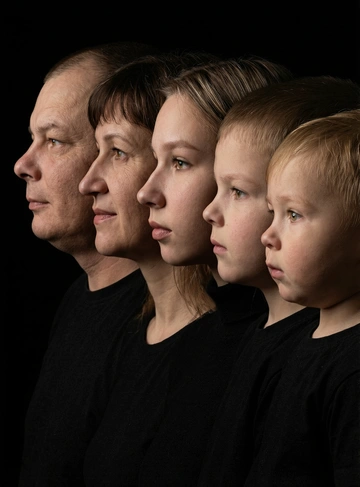 Профессиональный студийный портрет с низким контрастным светом. Головы расположены строго в одну линию. боковой профиль, взгляд влево. У всех видны только головы и немного плечи. Головы занимают весь кадр. Черный фон. Черная одежда у всех. Расположи их в таком порядке: папа, мама , девушка, ребенок, малыш