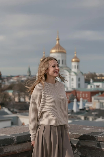 Женщина в свитере и длинной юбке стоит на крыше в центре Петербурга, позади видно купола Спаса на Крови и крыши города. Она улыбается и смотрит вдаль, волосы развеваются на ветру. Крупный план, атмосферный стиль.