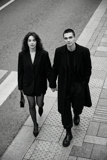 Черно-белая художественная фотография, ультрареализм, 8K, профессиональная съёмка; (оба): в кадре мужчина и женщина; каждый персонаж жёстко привязан к своему загруженному референсу, лица используются напрямую, без генерации, усреднения, подмены или смешения. Вид сверху под углом. Они идут по городской улице, держась за руки; шаг в движении, эффект «пойманного кадра». Смотрим вверх в камеру, выражение спокойное, уверенное, отстранённое.
Полностью чёрные образы modern classic: женщина — оверсайз-пиджак, короткое платье/юбка, плотные колготки, остроносые каблуки, маленькая сумка; мужчина — длинное пальто, свободный костюм, массивные ботинки.
Фон: асфальт, плитка, тактильная дорожка, геометрия.
Контрастный свет, мягкие тени, высокая детализация тканей.
Стиль: black & white, cinematic, high fashion, editorial, minimalism, street photography.
Качество: ultra high resolution, sharp focus, film grain, без ретуши.