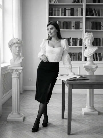   Взрослая девушка европейской внешности, около 30 лет, с аккуратной прической, одетая в белый топ, черную юбку миди с разрезом и черные копроновые чулки и черные туфли на каблуке. Сохрани лицо и черты лица с оригинального фото на 100%. Стоит и опирается на открытую книгу, ее взгляд направлен в сторону. На лице спокойное выражение, слегка лукавое. Рядом с ней находятся два мраморных бюста.
Интерьер кабинета. Стены светлые, на заднем плане стеллаж с книгами. На полу светлый паркет. Два мраморных бюста стоят на пьедесталах. Создается ощущение уединенности и спокойной атмосферы.
Чёрно-белая аналоговая фотография, классический портрет. Преобладает высокая детализация и контраст, придающие изображению глубину и драматизм.
Мягкий, рассеянный свет, вероятно, из окна, создающий плавные тени. Общее освещение хорошо подчеркивает текстуру тканей и мрамора. Средний план, композиция симметричная. Объект находится в центре кадра. Камера установлена на уровне глаз. Использование глубины резкости подчеркивает главного героя и детали интерьера.
