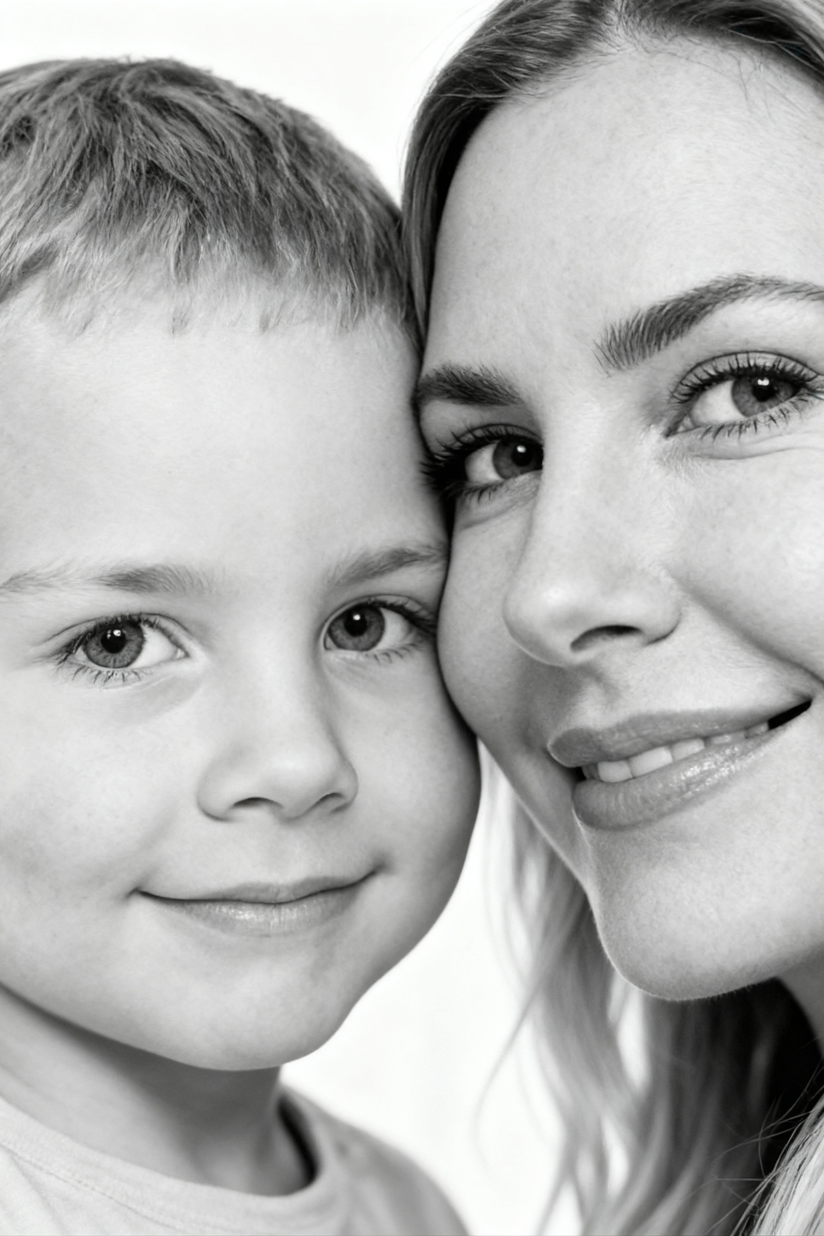 Сверхреалистичная черно-белая художественная фотография 8K женщины и ребенка, снятая очень крупным планом, щека к щеке так что видны только правая половина лица женщины и левая половина лица ребенка. которые смотрят в камеру. Их лица расположены рядом, почти соприкасаясь, образуя идеально сбалансированную симметричную композицию. Каждая деталь передана с фотографической точностью: тонкая текстура кожи и плавные градиенты света и тени. Видимая половина женщины включает ее бровь, один глаз , часть ее носа, щеку и губы, слегка приоткрытые в нежной, естественной улыбке, Видимая половина ребенка включает один глаз , круглую мягкую щеку, часть носа и небольшую улыбку, Фон белый и слегка размытый, что подчеркивает эмоциональную близость между ними. Освещение мягкое и рассеянное, создает деликатный контраст и тональную глубину. На снимке запечатлены нежность, близость и связь между матерью и ребенком, запечатленные с потрясающей реалистичностью. Не меняй черты лиц. 