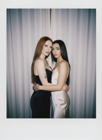 Take a picture with a Polaroid camera. the photo should look like a normal photo, without any clear subject or props. The photo should have a consistent light source such as a flash from a dark room, spread throughout the photo. Do not change the faces. Replace the background behind the two people with a white curtain. Люди на фото обнимаются. Две девушки одеты в платье-комбинации  