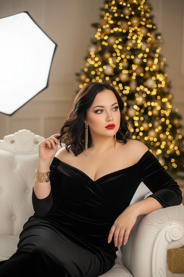 
Фотосессия в студии. Женщина сидит на белом диване на фоне украшенной только жёлтыми огоньками ёлки. Яркий макияж: красные губы и smokey eyes. Она одета в чёрное бархатное платье с открытыми плечами, носит золотой браслет и длинные серьги. Женщина позирует томно и изящно. Освещение от белого софтбокса, мягкое и рассеянное, создаёт уютную атмосферу. Светлые огоньки на ёлке образуют боке, добавляя праздничное настроение. Атмосфера романтичная и немного загадочная. Сидит с прямой спиной, одна рука опущена вдоль тела, другая играет с локоном. Голова слегка наклонена набок, взгляд мечтательный.