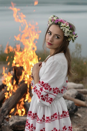 Девушка стоит спиной к тёплому костру, ближе к воде, на ней белое хлопковое платье с узором из красной вышивки по подолу и рукавам, венок из полевых цветов украшает её волосы. Она склонила голову к плечу, смотрит прямо в камеру, руки сложены на груди.