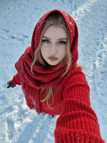       Не меняй черты лица  кинематографичный зимний портрет молодой женщины, селфи‑ракурс сверху, вертикальный кадр 9:16. камера смотрит почти строго вниз, девушка тянет руку к объективу. у неё очень светлая ровная кожа, глаза с длинными ресницами, аккуратные густые брови, нюдовый макияж, матовые розово‑припылённые губы.
она одета в ярко‑красный вязаный свитер и объёмный красный шерстяной шарф, накинутый на голову как капюшон/платок, на ткани заметны крупинки снега. светлые волосы частично спрятаны под шарфом, несколько прядей выбиваются по краям. фон — заснеженная земля с отпечатками следов и неровной коркой снега, холодные голубовато‑серые тона.
жёсткий зимний дневной свет, лёгкие синеватые тени, контраст тёплого красного и холодного снега, эффект живого селфи, ultra HD, high detail, realistic skin, snow and knit texture, cinematic lighting, top‑down selfie angle, vertical 9:16. 