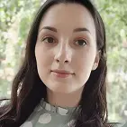 Женщина с тёмными волосами в платье в белый горох, на фоне зелёных деревьев.